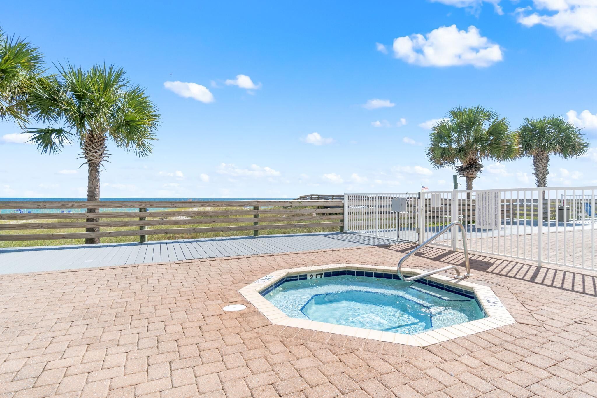 A pool area with a hot tub, wooden deck, and palm trees.