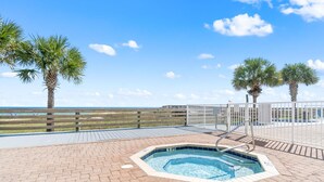 A pool area with a hot tub, wooden deck, and palm trees. - Seaspray Riverside 112 (Pensacola)