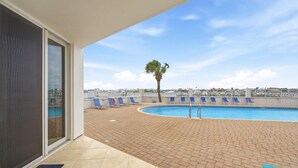 A pool area with blue lounge chairs, a palm tree, and a clear sky. - Seaspray Riverside 112 (Pensacola)