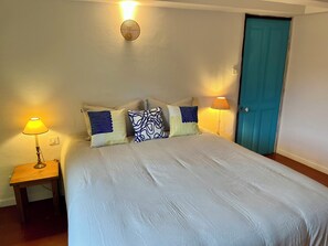 Een slaapkamer met een bed, twee bedlampjes, een wandlamp en een blauwe deur.