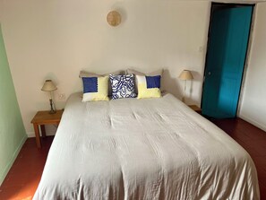 Une chambre à coucher avec un grand lit, deux tables de chevet, une porte bleue et un luminaire fixé au mur.