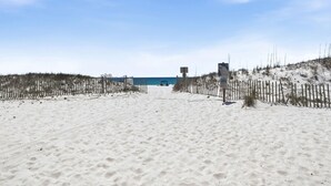 En sandstrand med ett trästaket, en livräddartorn och en byggnad i bakgrunden.
