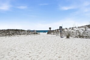 A sandy beach with a wooden fence, a lifeguard tower, and a building in the background. - The Doc Beach House (Gulf Shores)