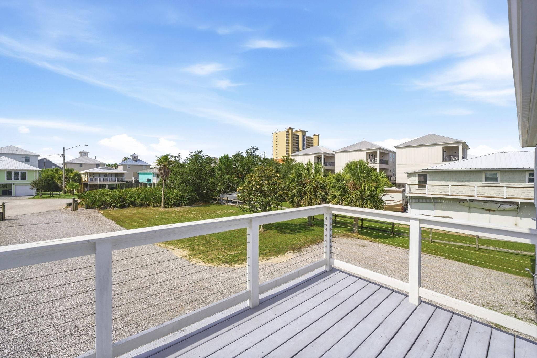 A wooden deck with a white railing, a grassy area, and buildings in the background.