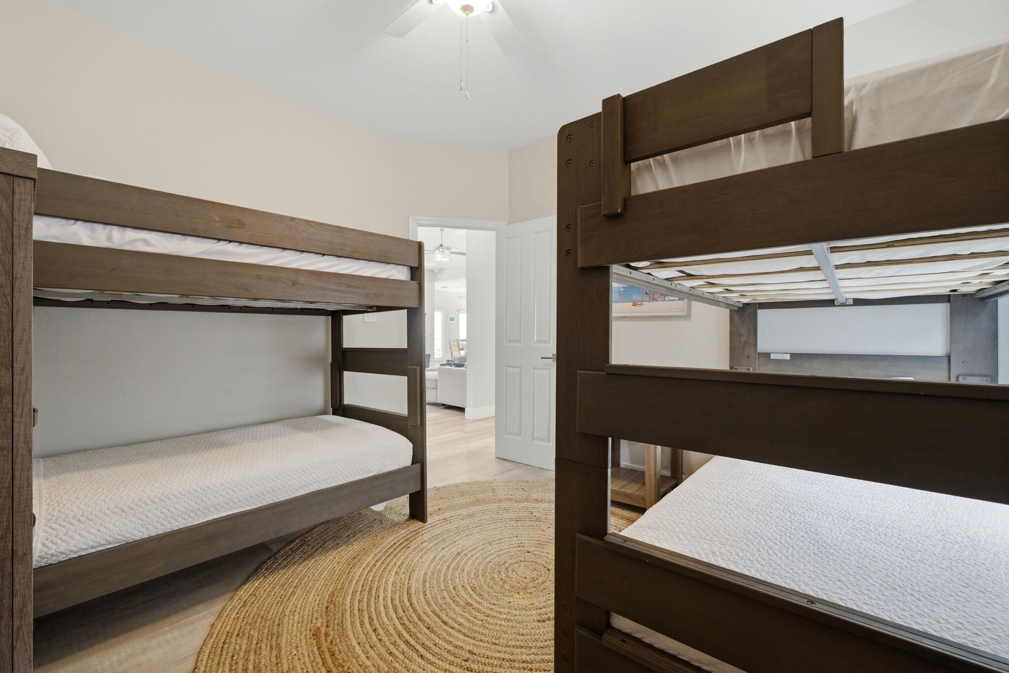 Habitación con literas, un tapete tejido y una puerta que da a otra habitación.