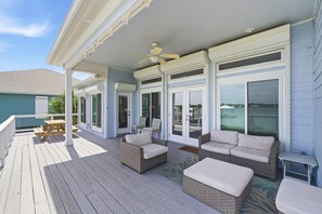 A covered outdoor deck with wicker furniture, a ceiling fan, and sliding glass doors. - The Doc Beach House (Gulf Shores)