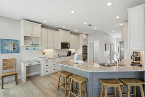 A modern kitchen with white cabinetry, a granite countertop, and wooden stools. - The Doc Beach House (Gulf Shores)
