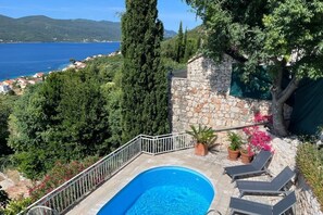 Una piscina con muro in pietra, lettini e vista sul mare e sulle colline.