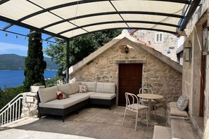 Una terrazza con tetto in pietra, con divano, sedie e tavolo, affacciata su un lago e delle colline.