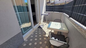 Un piccolo patio esterno con tavolo e sedie in vetro, una stendibiancheria in metallo e un pavimento piastrellato.
