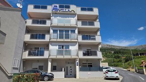 Ein mehrstöckiges Hotel mit Balkonen, einem Schild mit der Aufschrift 'AB VILLA' und einer Bergkulisse.