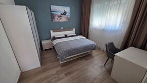 Ein Schlafzimmer mit Bett, Schreibtisch, Stuhl, Nachttisch, Kommode und einem Bild an der Wand.