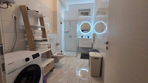 Un bagno moderno con lavatrice, servizi igienici e cabina doccia in vetro.
