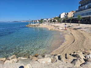 Un hotel sul lungomare con vista sul mare cristallino, una spiaggia di ciottoli e un litorale roccioso.