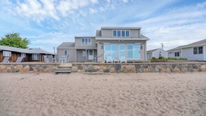A beachfront property with a large house featuring a stone retaining wall, a covered patio, and a view of the ocean.
