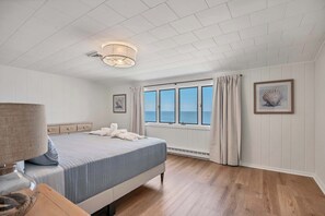 A bedroom with a bed, a bedside table, a lamp, a window with curtains, and a framed picture on the wall.
