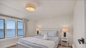 A bedroom with a bed, bedside lamps, a nightstand, a window with a view of the sea, and a ceiling light fixture.