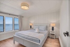 Ein Schlafzimmer mit Bett, Nachttischlampen, einem Nachttisch, einem Fenster mit Meerblick und einer Deckenleuchte.