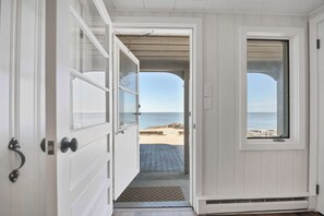 Une porte qui donne sur une plage, avec une terrasse en bois et un ciel dégagé.