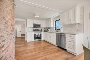 A modern kitchen with white cabinets, stainless steel appliances, and a wooden floor.