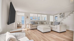 A modern living room with a sectional sofa, a flat-screen TV, and a staircase.