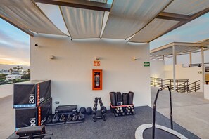 Un gimnasio en la azotea con equipo de ejercicio, incluyendo mancuernas, pesas rusas y un banco.