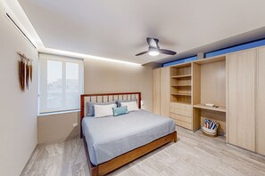 Un dormitorio con cama, ventilador de techo, ventana y estanterías de madera empotradas.