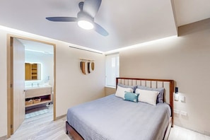 A bedroom with a bed, a ceiling fan, a nightstand, and a bathroom visible through an open door.