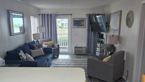 Uma sala de estar com sofá, um espaço de jantar com mesa e uma cozinha com armários.