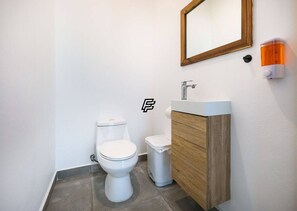 Ein modernes Badezimmer mit Toilette, Mülleimer, Waschbecken und Spiegel.