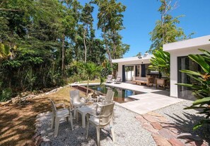 Ein modernes Haus mit Swimmingpool, Gartenmöbeln und üppiger Bepflanzung.