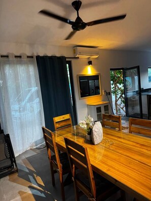 Ein Essbereich mit Holztisch, Stühlen, Deckenventilator, Klimaanlage und Blick ins Freie.