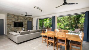 Un salon moderne avec un mur en pierre, un canapé gris, une table à manger en bois avec des chaises et un ventilateur de plafond.