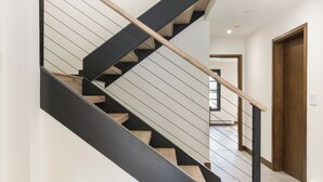 Eine moderne Treppe mit Holzwandlaufingen und schwarzen Stufen, die zu einem Raum mit einer weißen Tür und einem Fenster führt.
