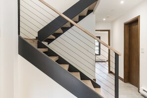 A modern staircase with a wooden handrail and black steps, leading to a room with a white door and a window. - Modern Mountain Home with Lux Kitchen & Cozy Living Room Heart of Beaver Creek (Beaver Creek)