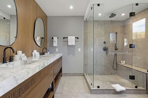 A modern bathroom with a marble vanity, a large mirror, a glass-enclosed shower, and a view of trees. - Modern Mountain Home with Lux Kitchen & Cozy Living Room Heart of Beaver Creek (Beaver Creek)