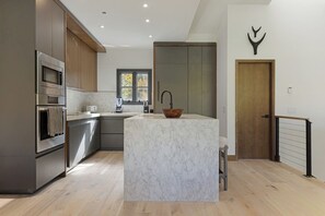 A modern kitchen with a marble island, stainless steel appliances, and a wooden door. - Modern Mountain Home with Lux Kitchen & Cozy Living Room Heart of Beaver Creek (Beaver Creek)