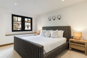 A bedroom with a large bed, a window with a view, a bedside table with a lamp, and wall-mounted antlers. - Modern Mountain Home with Lux Kitchen & Cozy Living Room Heart of Beaver Creek (Beaver Creek)