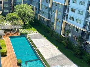 Un edificio residencial con piscina, mobiliario exterior y abundante vegetación.