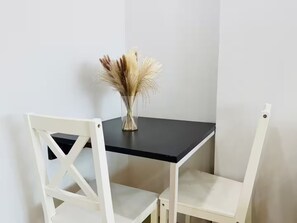 Una silla blanca con una mesa negra, un jarrón con plantas secas y una pared blanca lisa.