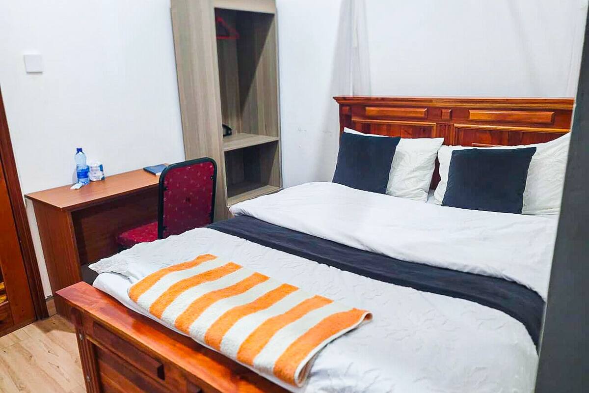 A hotel room with a bed, a desk, a chair, a wardrobe, and a window.