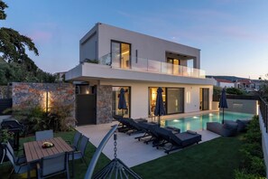 Une maison moderne à deux étages, dotée d’une piscine, d’un espace salon extérieur et d’un mur en pierre.
