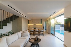 A modern living room with a sofa, dining table, chairs, and a staircase. - Green villas, perfect for relaxing family or friends’ vacations (Rethymno)