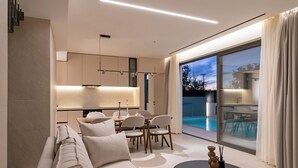 A modern living room with a sofa, dining table, chairs, and a pool view. - Green villas, perfect for relaxing family or friends’ vacations (Rethymno)