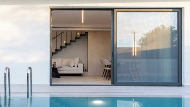 A modern poolside area with a clear view of a living room, a staircase, and a glass door leading to an outdoor space. - Green villas, perfect for relaxing family or friends’ vacations (Rethymno)