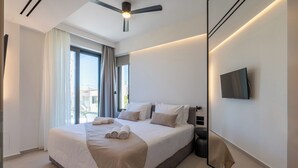 A modern hotel room with a large bed, a ceiling fan, a flat-screen TV, and a view of the outside. - Green villas, perfect for relaxing family or friends’ vacations (Rethymno)