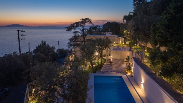 Ein Pool, eine Terrasse und Meerblick im Abendlicht.