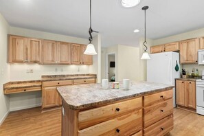 A kitchen with wooden cabinets, granite countertops, a central island with drawers, a refrigerator, and pendant lighting. - Spacious 4-Bedroom Cabin with Theater, Game Room, Fireplaces & Year-Round Views (Murphy)
