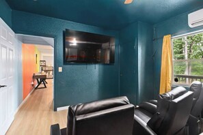 A room with teal walls, a mounted TV, leather seating, and a window with a view of trees. - Spacious 4-Bedroom Cabin with Theater, Game Room, Fireplaces & Year-Round Views (Murphy)