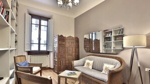 Een woonkamer met een bank, stoelen, een salontafel, een boekenkast, een spiegel en een vloerlamp.